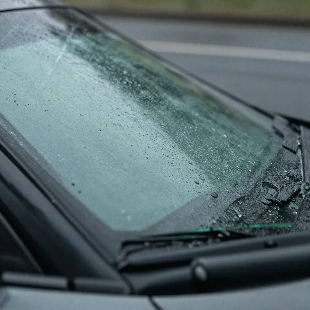 Close view of rain beading across the base of a freshly fitted windshield and its wiper blades